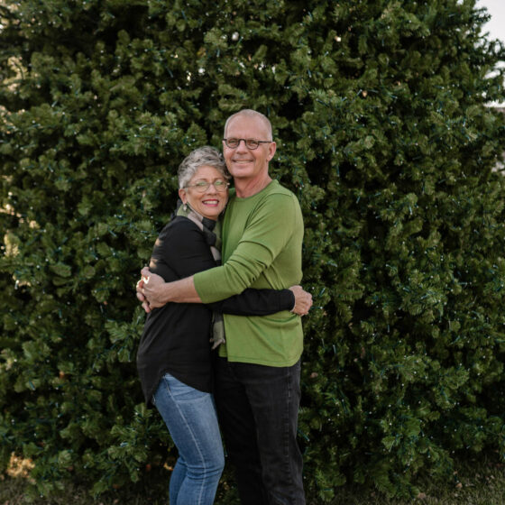 A couple hugs in front of a christmas tree