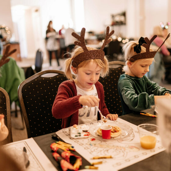 Two little girls wearing reindeer antlers decorate waffles