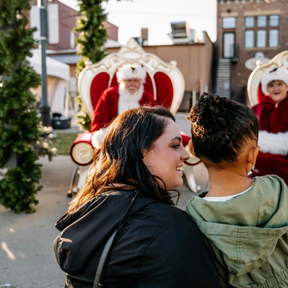 A little girl held by her mother meets santa and mrs clause