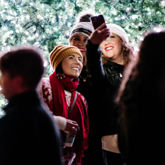 Two women hold a cell phone up for a selfie in front of a christmas tree