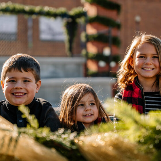 Three children smile in a Christmas decorated park