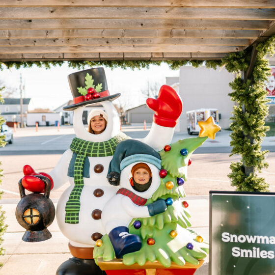 Two individuals pose behind a cut out snowman