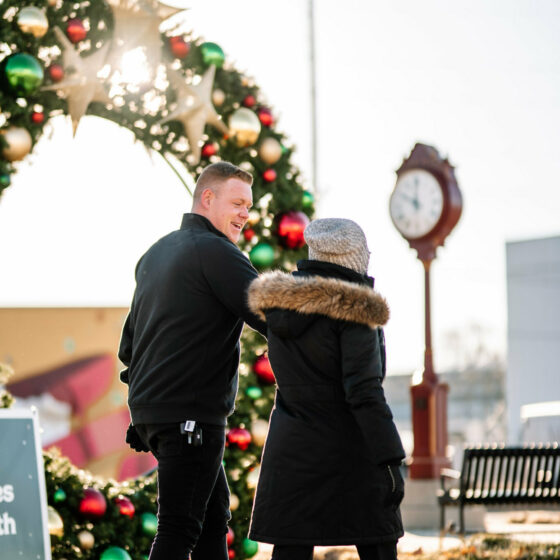 a couple strolls in front of a decorated arch at Christmas in Le Mars