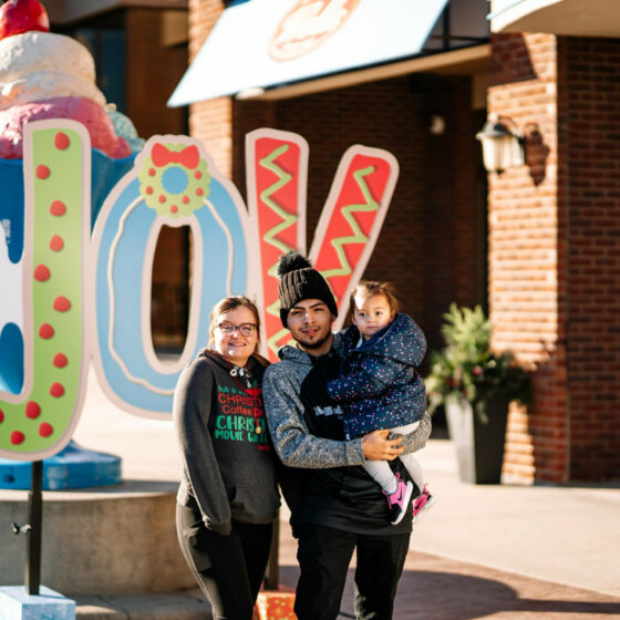 A young family stands in front of a Blue Bunny sign that says joy